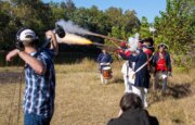 Shenandoah student Johnny Bernard holds a boom mic while members of the National Society of the Sons of the American Revolution fire a volley
