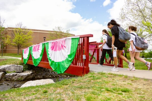 Shenandoah students walk across a bridge decorated with pink, white and green bunting.