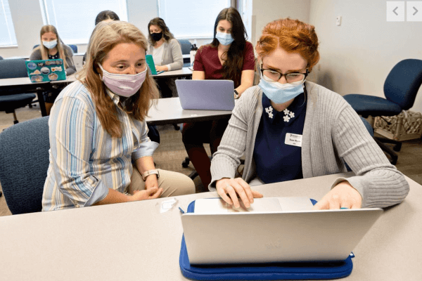 Shenandoah University Occupational Therapy Associate Professor Alicia Lutman, OTD, and OT student Tessa Myers, both masked and sitting at a desk, featured in a Northern Virginia Daily photo by Rich Cooley.