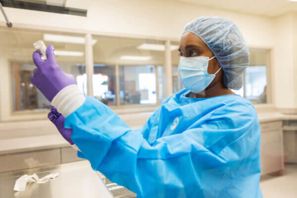 Shenandoah University Bernard J. Dunn School of Pharmacy student in blue scrubs, gloves, cap and mask, holding a vial.