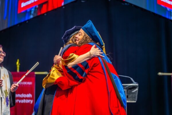 Shenandoah University's president shares a hug with a graduate on the commencement stage.