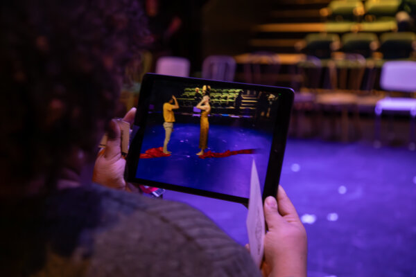 An audience members uses an iPad to watch virtual dancers perform on-stage in Glaize Studio Theatre