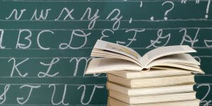 Stock image of books in front of cursive alphabet letters on a blackboard.