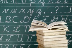 Stock image of books in front of cursive alphabet letters on a blackboard.