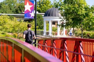Shenandoah University campus, student walking over a red bridge.