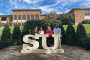Shenandoah University's Staci Strobl, Cardiff University's Samantha Buzzard, and Shenandoah's Karrin Lukacs and Younus Mirza pose at the SU statue on the university's main campus
