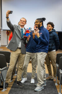 Shenandoah University students take a selfie with a Buzzy plush toy during a send-off event for an experiential learning trip to Arizona for Super Bowl LVII