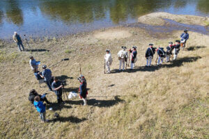 A group of Shenandoah University students, faculty and staff and members of the National Society of the Sons of the American Revolution stand along the bank of the Shenandoah River during the filming of training videos for the SAR