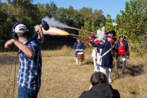 Shenandoah student Johnny Bernard holds a boom mic while members of the National Society of the Sons of the American Revolution fire a volley