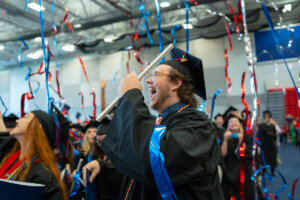 A Shenandoah University graduate celebrates as red, white and blue streamers fall from the ceiling at the end of Commencement 2023