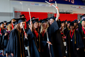 Students in caps and gowns lift their diplomas in celebration during Shenandoah University's 2022 Commencement