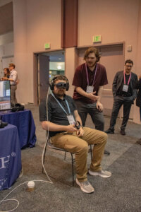 Shenandoah University student Luke Yager assists an individual wearing a VR headset at SU's booth at the Augmented World Expo