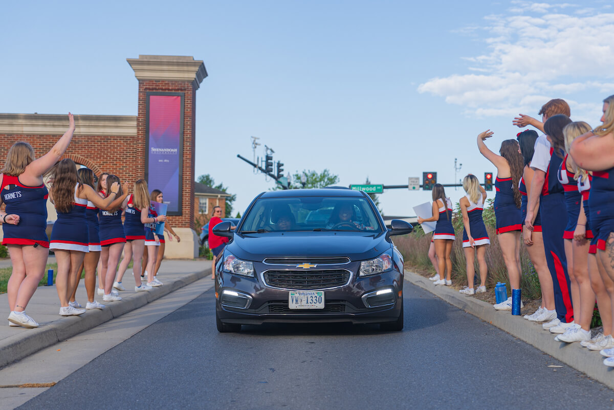 Car arriving on campus, flanked by cheerleaders on Move-In Day 2023