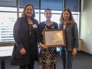 Shenandoah University's Audra Gollenberg holds a framed award while standing alongside Interim Provost Karen Abraham and Shenandoah University President Tracy Fitzsimmons