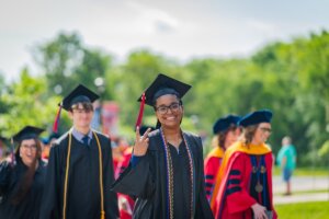 A Shenandoah University graduate holds up the "peace" sign as they process to the 2023 University Commencement ceremony.