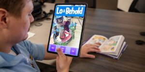 A person holds a tablet demonstrating the "Lo and Behold" augmented reality companion app.