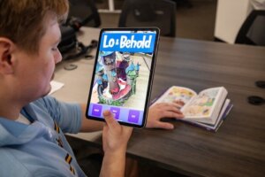 A person holds a tablet demonstrating the "Lo and Behold" augmented reality companion app.