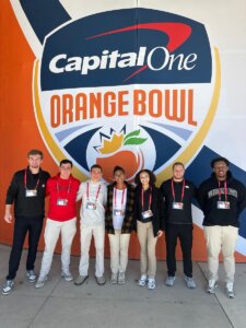 Shenandoah University students pose for a photo in front of the Capital One Orange Bowl logo.