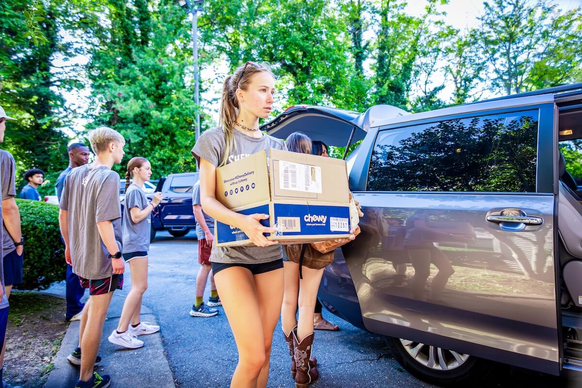 A Shenandoah University student-athlete carries a box from a vehicle.