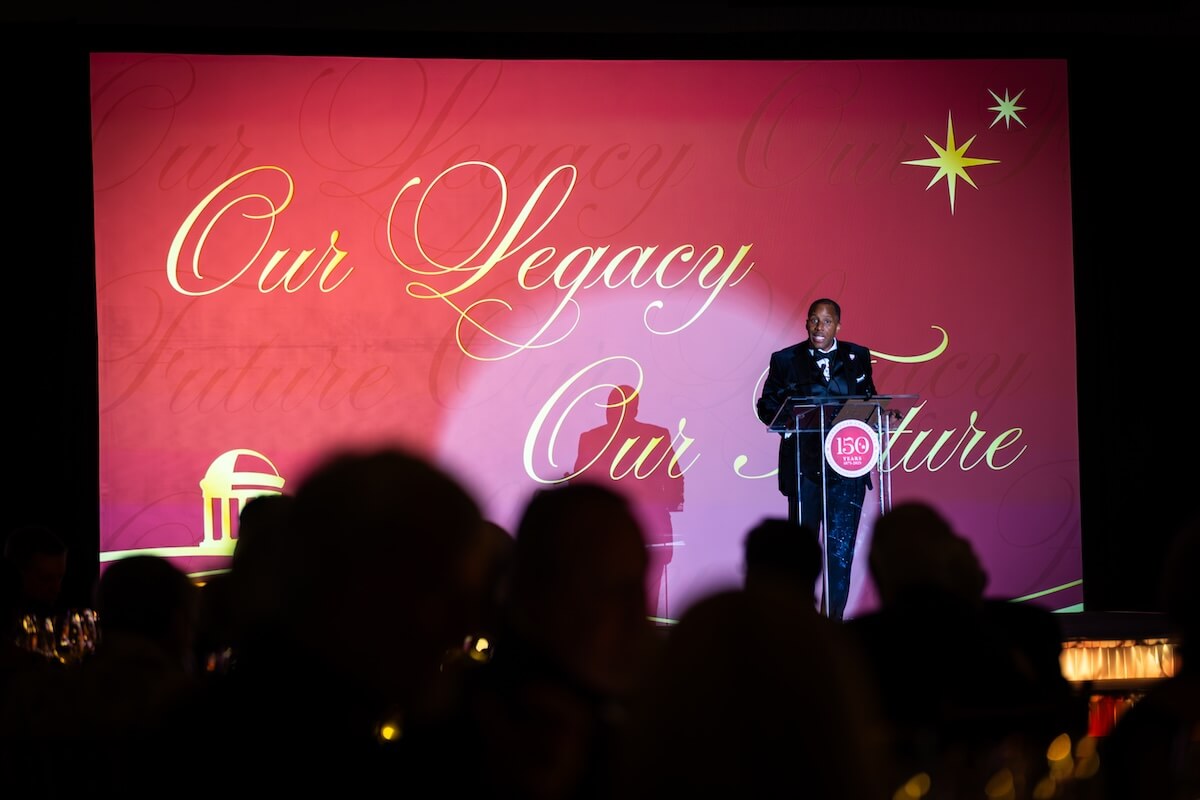 James Imoh speaks at a podium against a backdrop that reads "Our Legacy, Our Future."