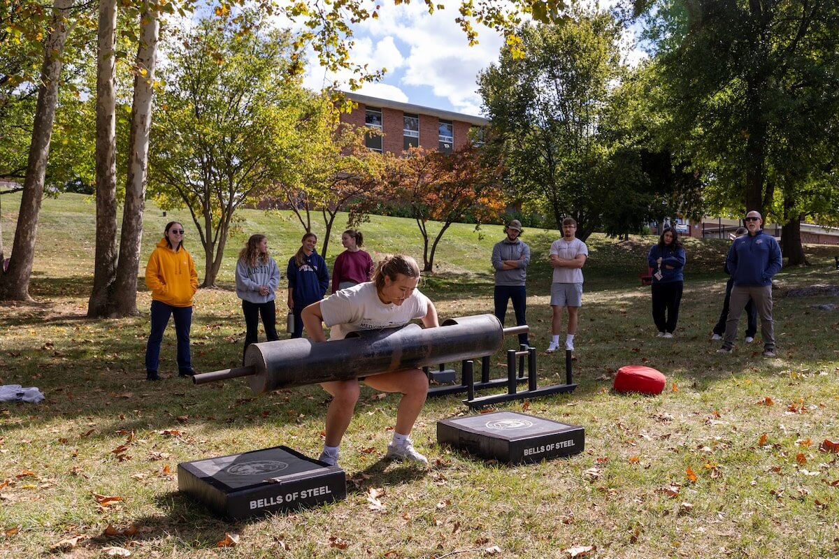 Shenandoah University student Sophia Sharp '27 shows off her strongwoman skills lifting the Bells of Steel on the campus Quad during fall 2025.