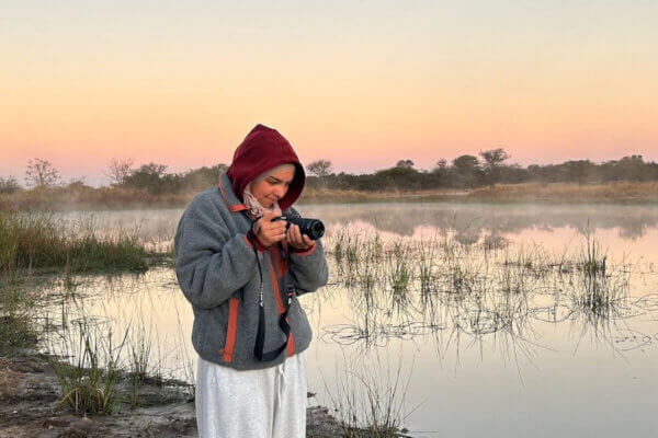 Jennah Elganainy takes a photograph in wetlands with a sunset sky in the background.