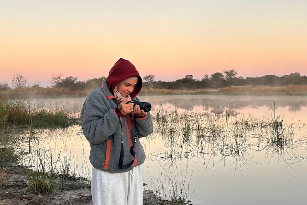 Jennah Elganainy takes a photograph in wetlands with a sunset sky in the background.