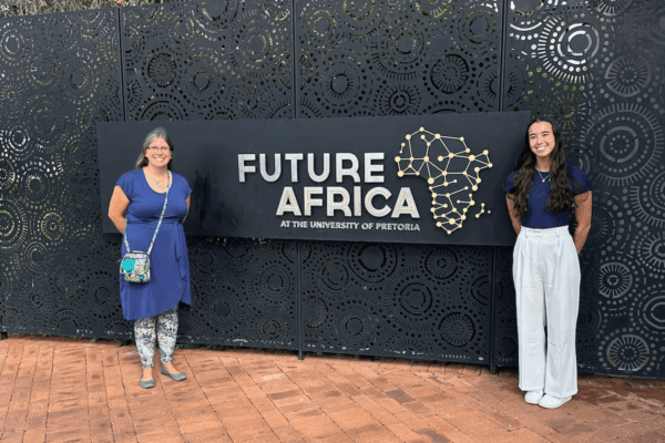 Camilla Hollen and Zoe Star stand with a sign for the Future Africa Campus at the University of Pretoria in South Africa.