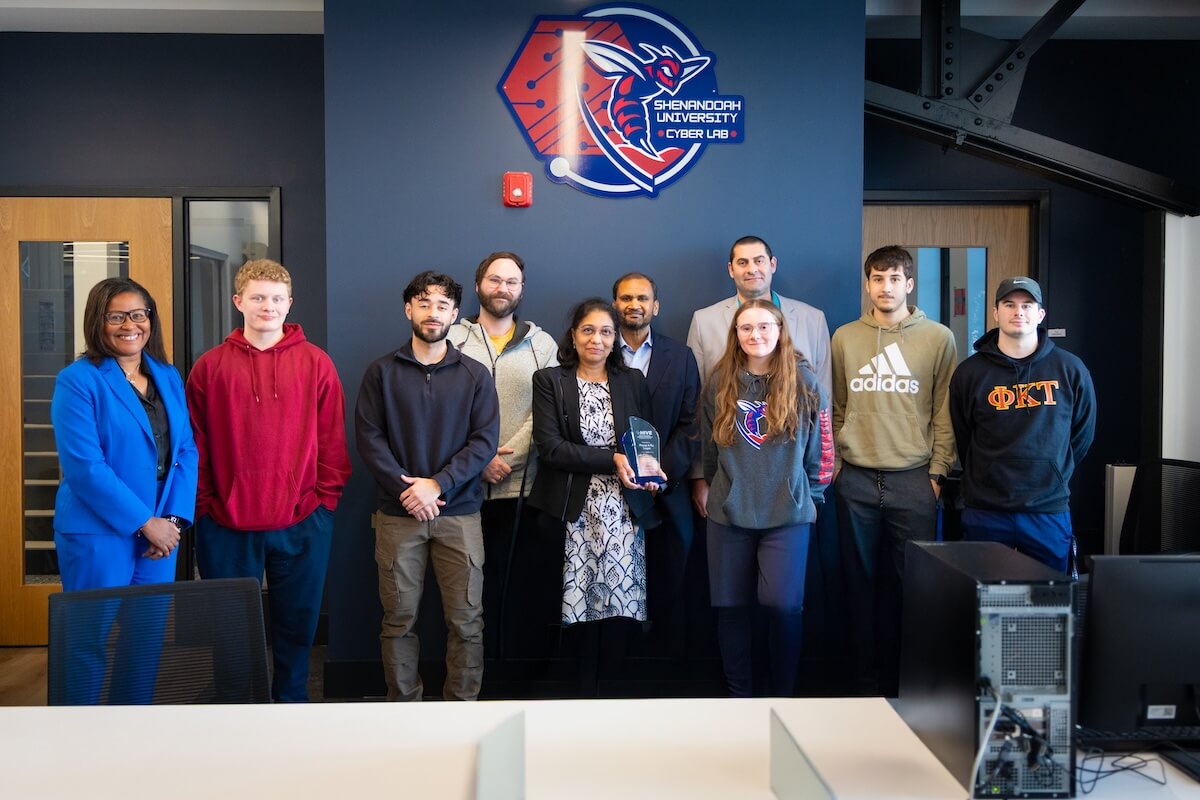 Students, faculty and staff pose with Raj and Neeraja Lingam beneath a logo for the cybersecurity lab.