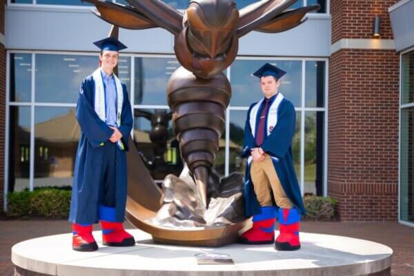 Shenandoah students pose in graduation regalia and Buzzy mascot feet.