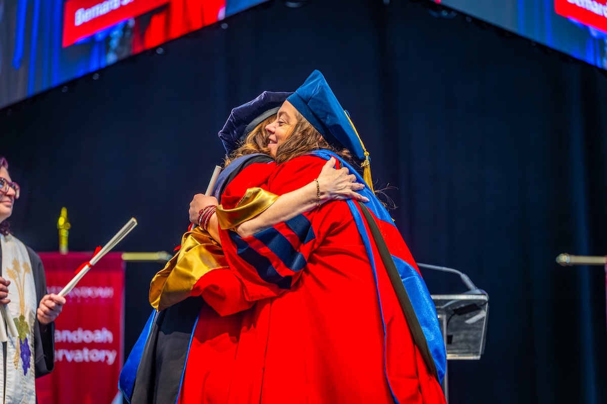 Shenandoah University's president shares a hug with a graduate on the commencement stage.