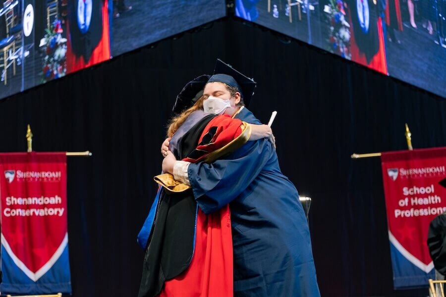 A student hugs Shenandoah president Tracy Fitzsimmons on stage during commencement.