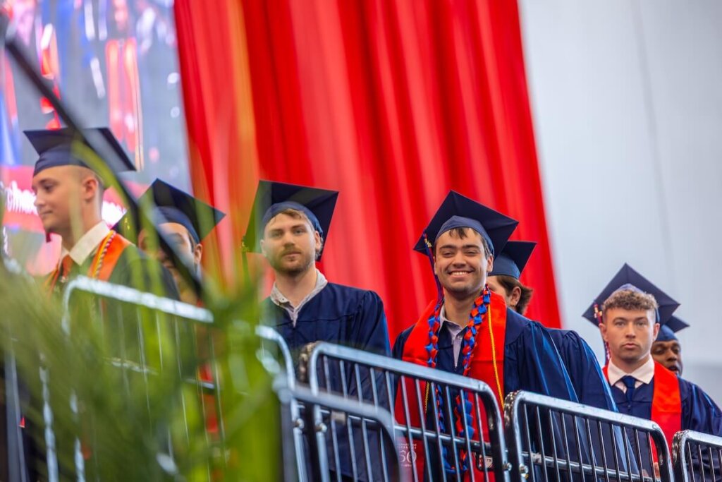 James Wilkins IV smiling at the camera as he waits with fellow graduates to cross the stage.
