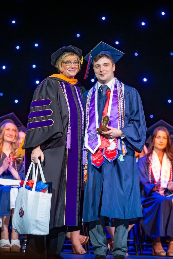 Dylan Hill in graduation regalia during the Eleanor Wade Custer School of Nursing's pinning and hooding ceremony.