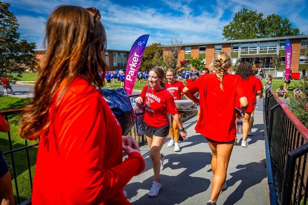 Softball student-athletes carry items into a residence hall.
