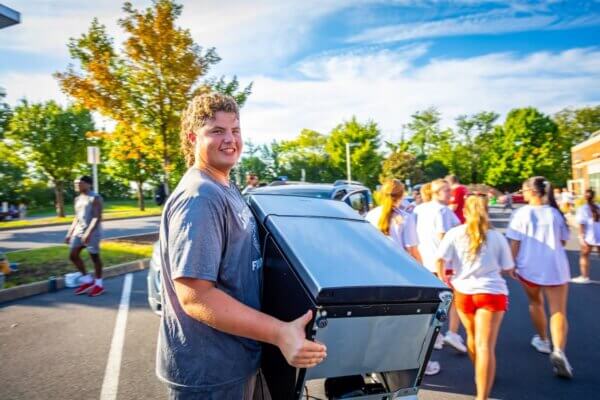 A football student-athlete carries a mini fridge.