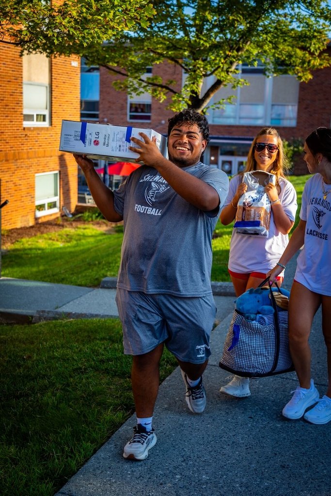 A student-athlete carries a large box on their shoulder.