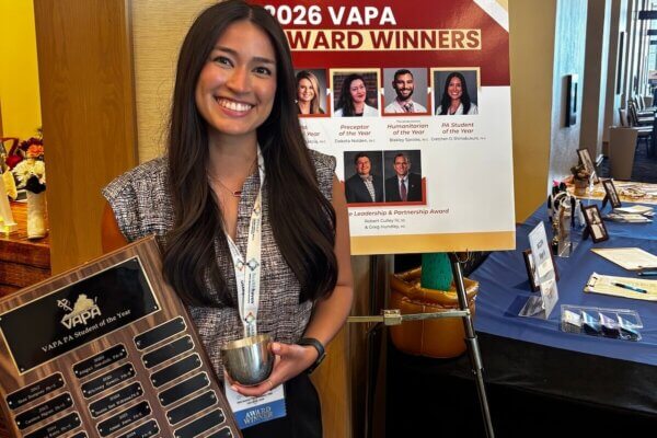 Gretchen Olazabal Shimabukuro ’26, a Shenandoah University physician assistant studies student, is the 2026 Virginia Academy of Physician Assistants’ PA Student of the Year, holding the award plaque with her name on it and standing in front of a poster with all the year's VAPA winners on it.