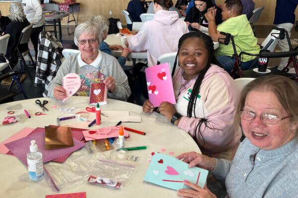 A Shenandoah student sits at a table with two older adults as they make Valentine's Day cards.