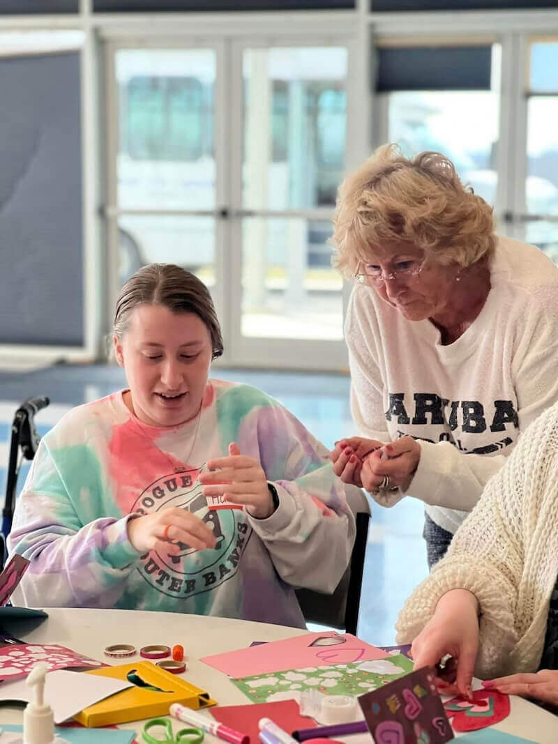A Shenandoah student interacts with an older woman as they look at a table full of crafting supplies.