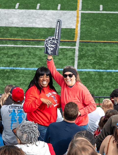 Two women at homecoming cheering at a football game