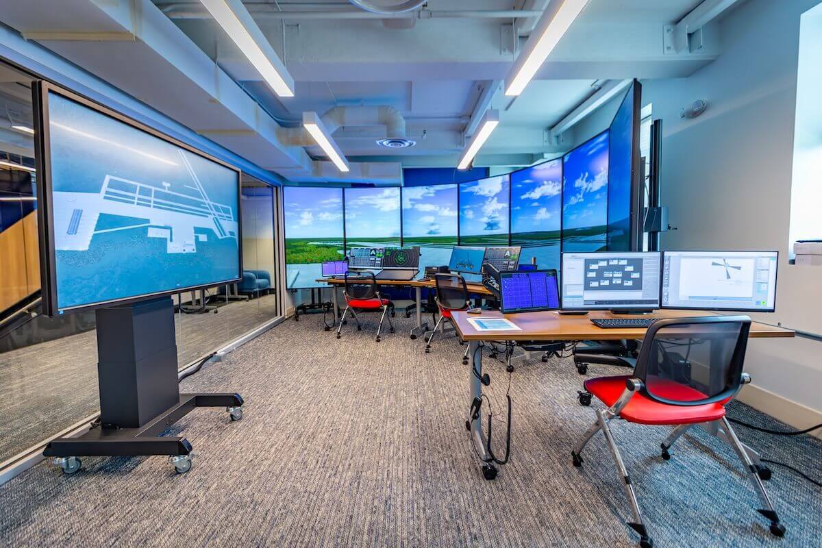 An air traffic control simulator lab featuring large screens, computer monitors.