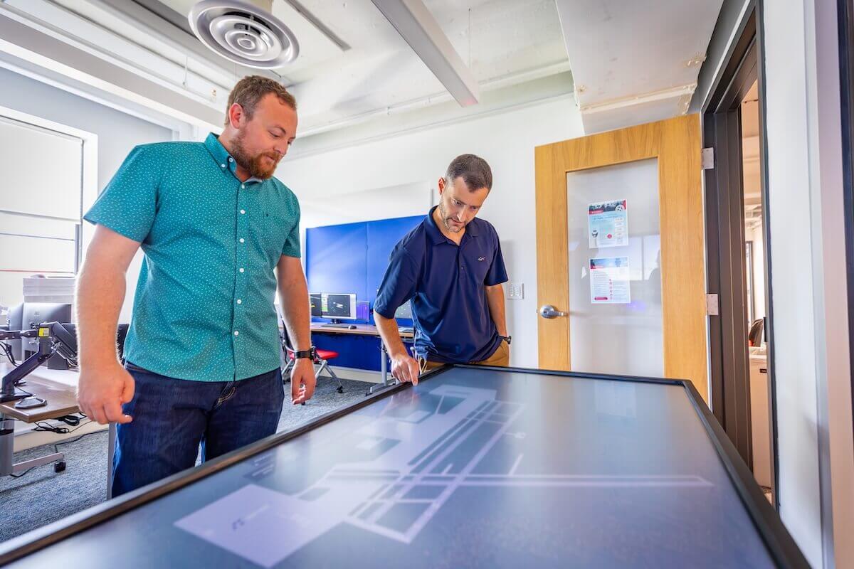 Two individuals examine a touchscreen table in the air traffic control simulation lab.