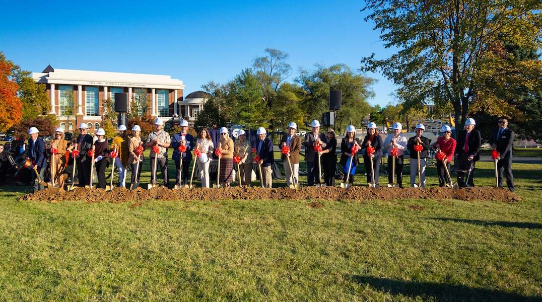 A large group of individuals wear hardhats and hold shovels during the groundbreaking for the Dove Center for the Arts.