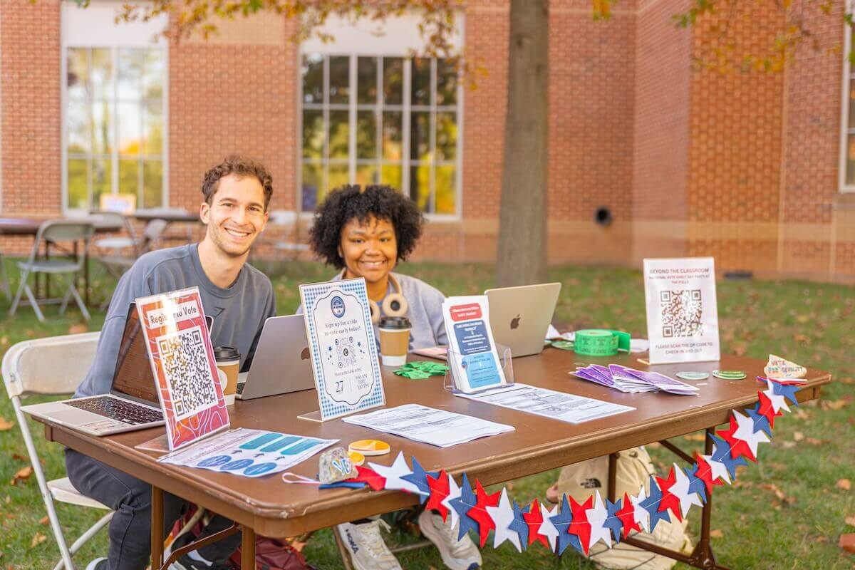 Two Shenandoah students sit at an outdoor table full of voter education materials.