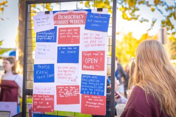 A sign displays handwritten responses to the phrase "democracy works when..." on red, white and blue paper.