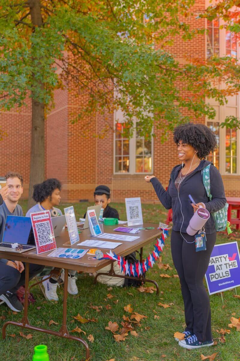 A student approaches an outdoor table full of voter education materials.