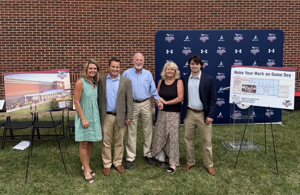 Members of the Wilkins family stand between posters showing the planned expansion of the Wilkins Athletics and Events Center.